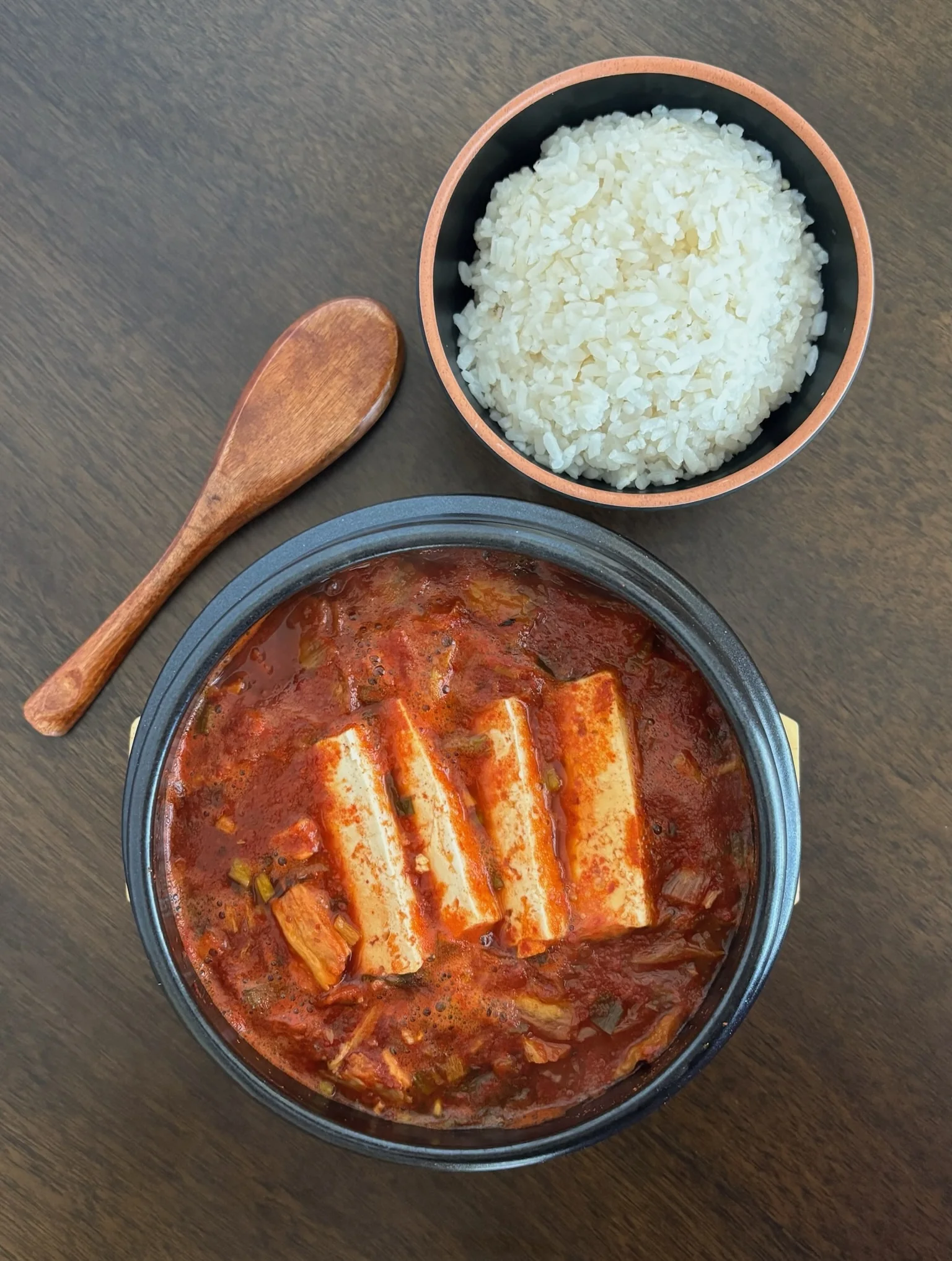Finished kimchi jjigae with tofu in a black bowl, served with steamed rice