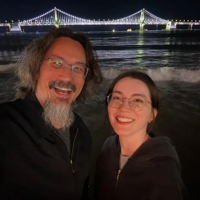 John and Fiona smiling beside an illuminated bridge during their 2025 trip to Korea