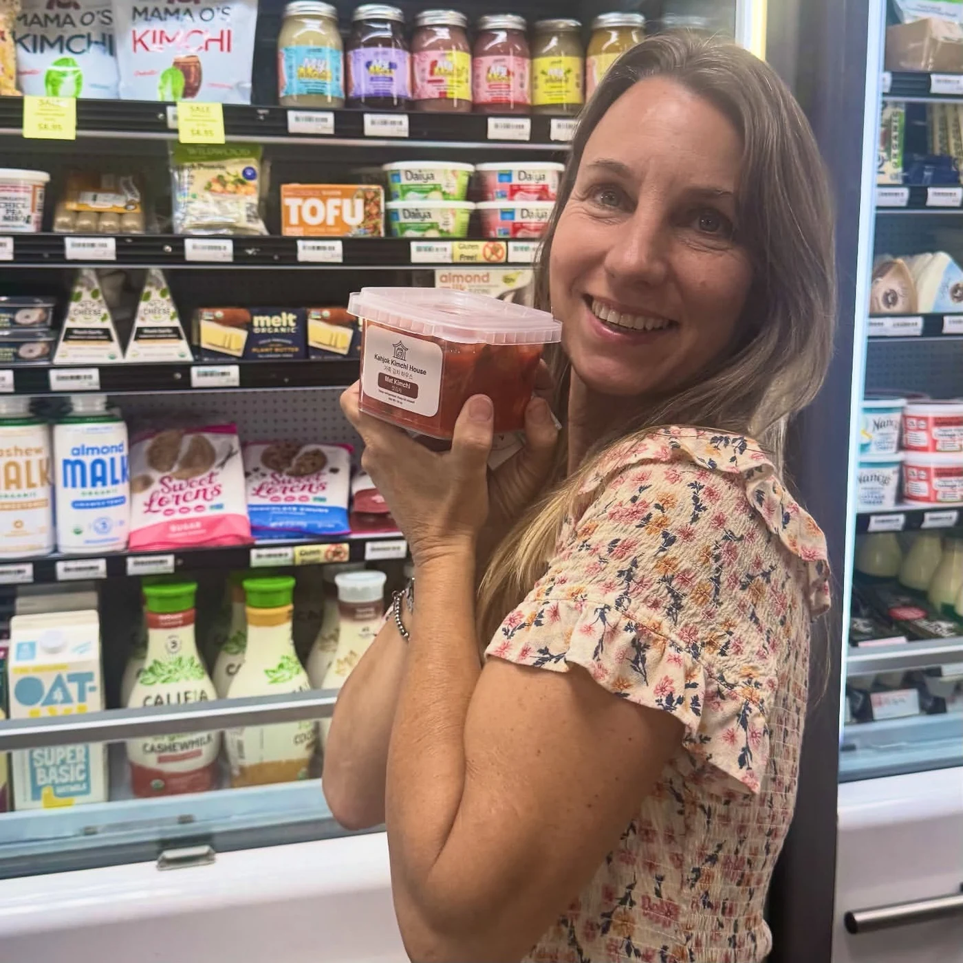 Tonya, Naturals Manager at Village Foods & Pharmacy in Bryan, Texas, holding a jar of Kahjok Kimchi House mat kimchi