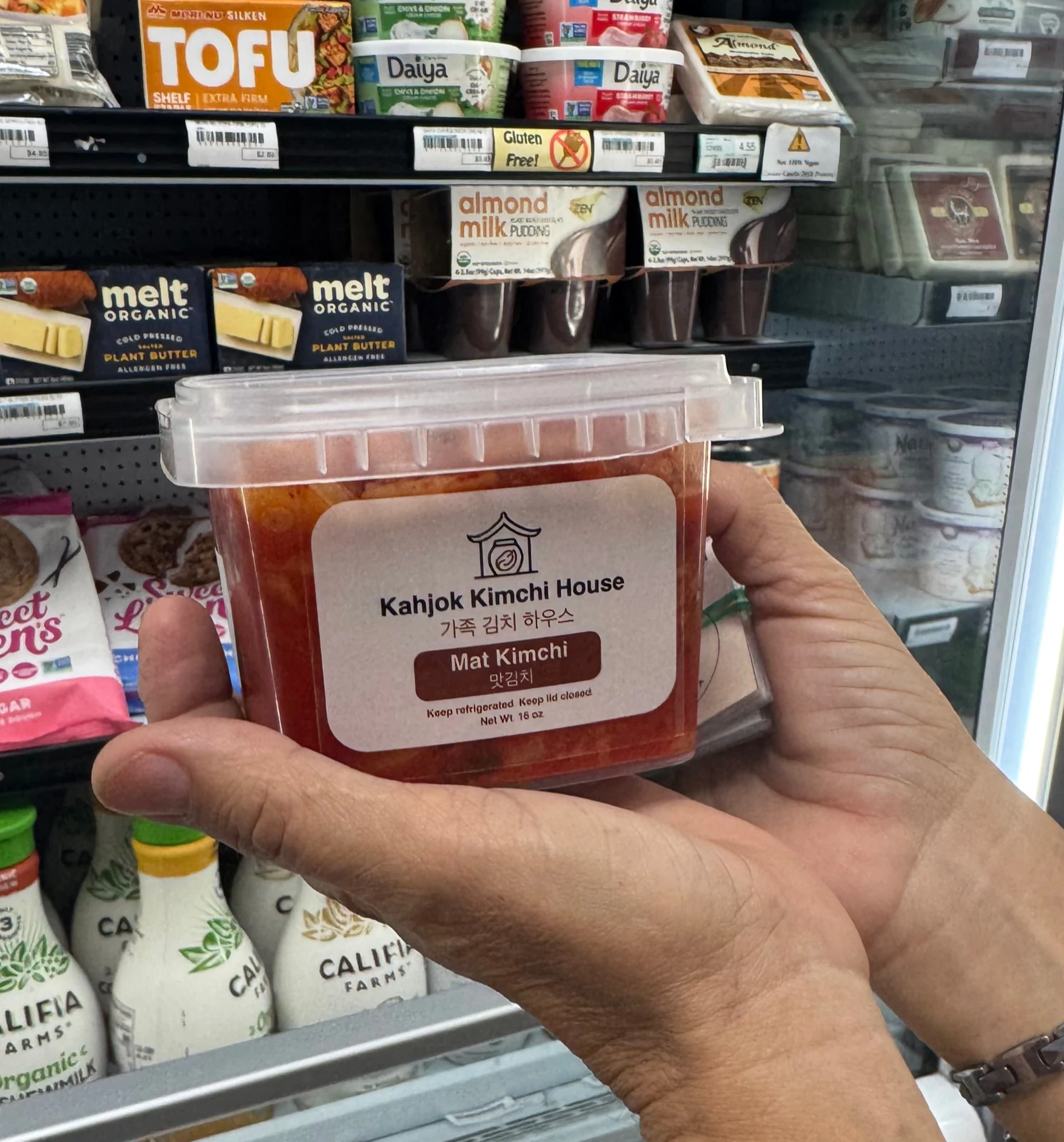 A hand holding a jar of Kahjok Kimchi House's mat kimchi at Village Foods & Pharmacy in Bryan, Texas